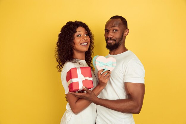 Geschenkboxen halten. Valentinstagfeier, glückliches Afroamerikanerpaar lokalisiert auf gelbem Studiohintergrund.