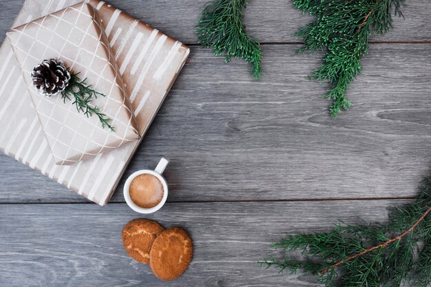 Geschenke in der Nähe von Zweigen, Tasse Getränk und Kekse