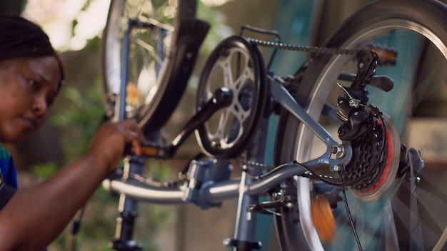 Kostenloses Foto geschickte junge schwarze frau führt wartungsarbeiten am fahrrad durch, repariert selbstbewusst die kette und inspiziert den kurbelarm. afroamerikanische dame prüft auf zu reparierende schäden, nahaufnahme von fahrradteilen.