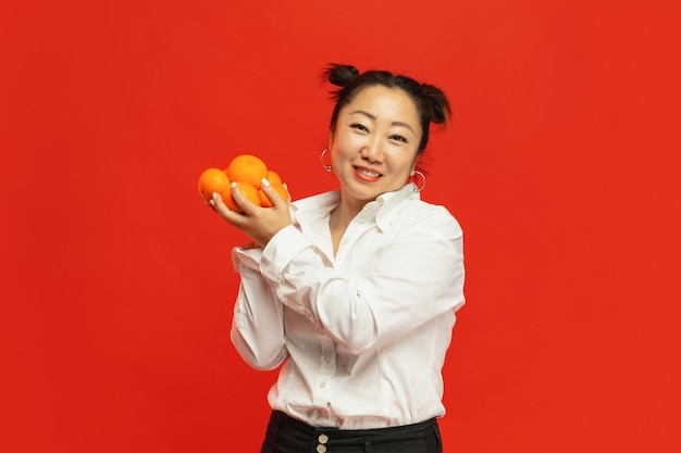 Geschmack der Ferien. Frohes chinesisches neues Jahr 2020. Asiatische junge Frau, die Mandarinen auf rotem Hintergrund in traditioneller Kleidung hält.
