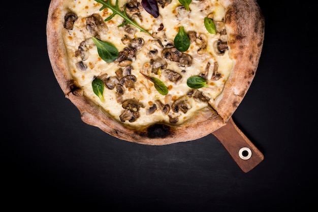 Geschmackvolle käsige Pilzpizza und -basilikum verlässt auf hölzernem Brett über schwarzem Hintergrund