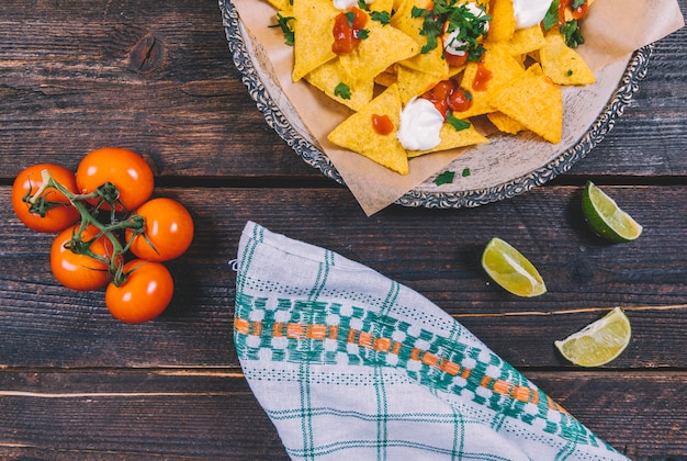 Kostenloses Foto geschmückte geschmackvolle mexikanische nachos in der platte mit zitronenscheiben und kirschtomaten auf braunem hölzernem schreibtisch