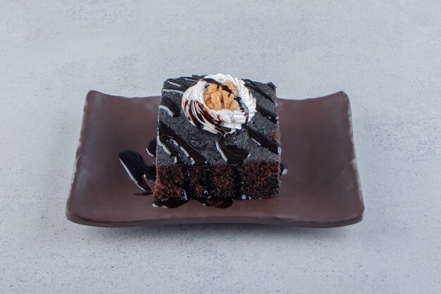 Geschnitten von leckerem Schokoladenbrownie mit Sahne auf dunklem Teller. Foto in hoher Qualität