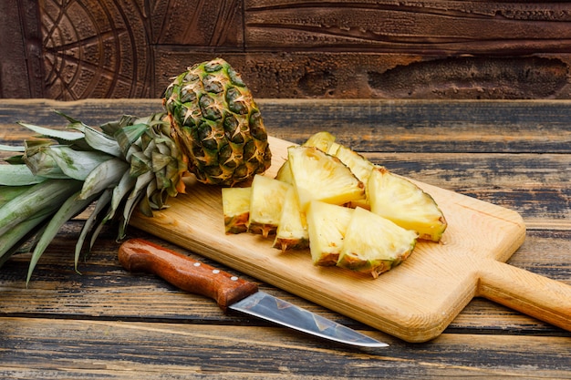 Geschnittene Ananas in einem Schneidebrett mit einer Obstmesserseitenansicht auf einer Holzschmutzfläche und einer Steinfliese