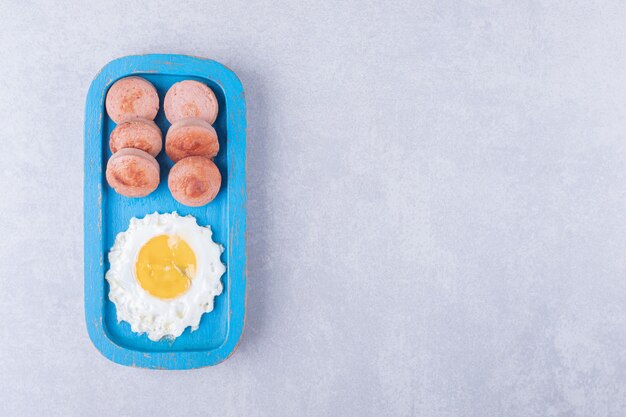 Geschnittene Bratwürste und Ei auf blauem Teller.