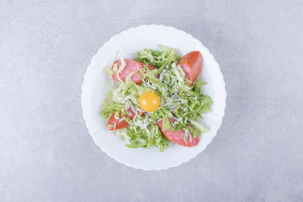 Geschnittene geräucherte Würste, Salat und Eigelb in weißer Schüssel.