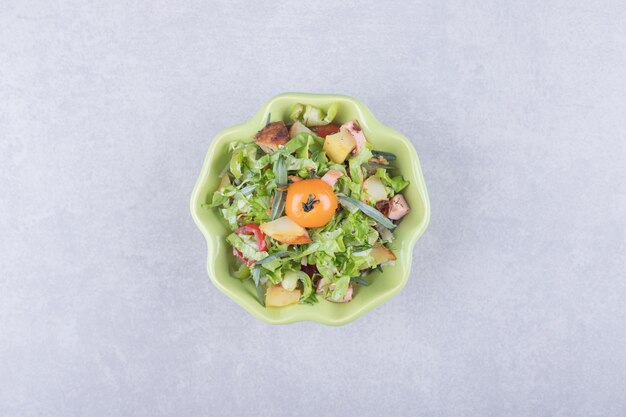 Geschnittene geräucherte Würste, Salat und Tomate in grüner Schüssel.