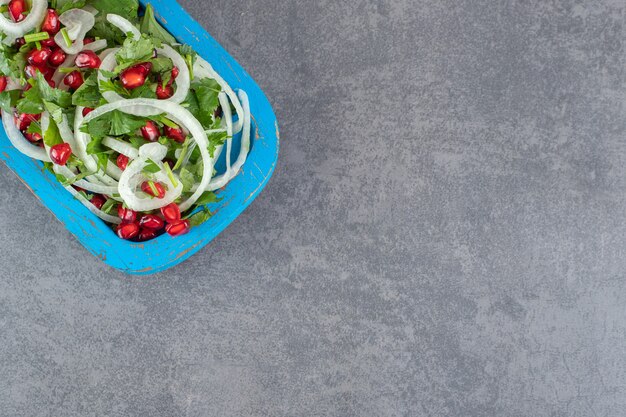 Geschnittene Grüns, Zwiebeln und Granatapfelkerne auf blauem Teller. Foto in hoher Qualität