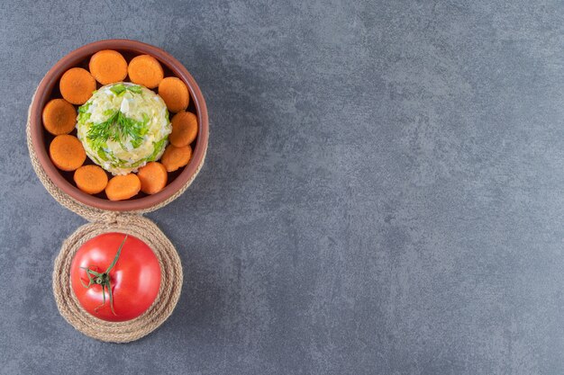 Geschnittene Karotten und Hauptsalat in einer Schüssel neben Tomaten auf Untersetzer auf der blauen Oberfläche