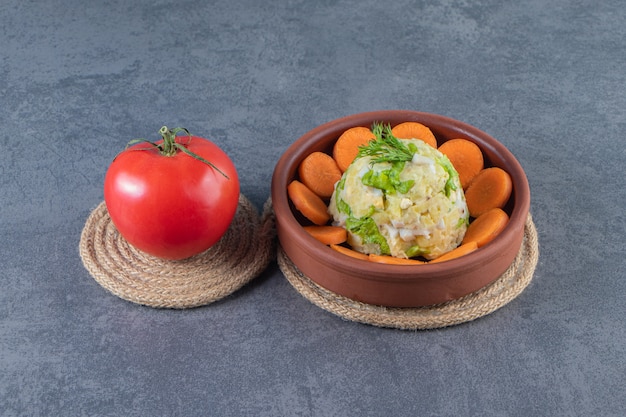 Geschnittene Karotten und Hauptsalat in einer Schüssel neben Tomaten auf Untersetzer auf der blauen Oberfläche