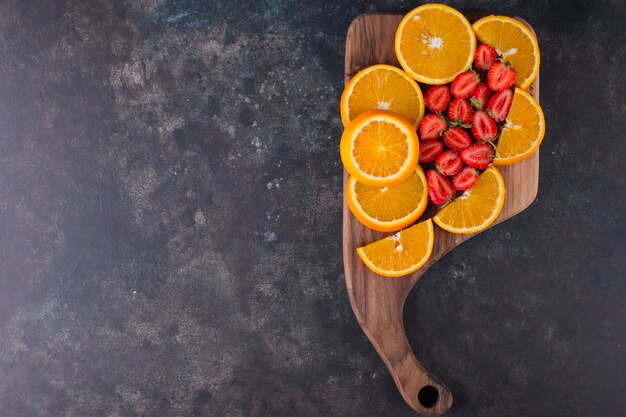 Geschnittene Orangen und Erdbeeren auf einem Holzbrett, Draufsicht