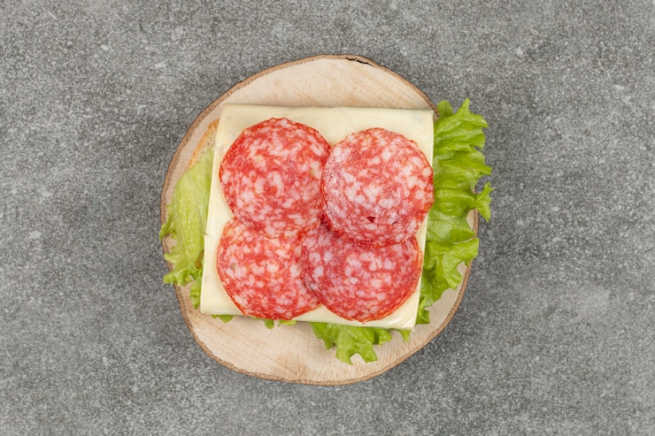 Kostenlose Foto geschnittene salami auf holzstück mit käse und salat