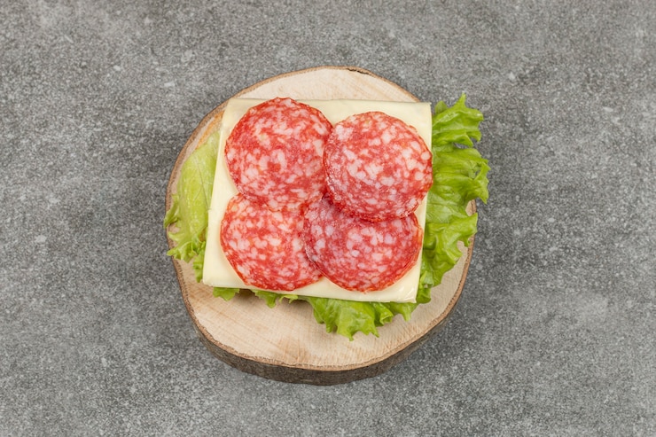 Kostenlose Foto geschnittene salami auf holzstück mit käse und salat