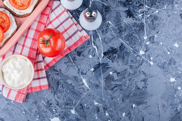 Geschnittene Tomaten auf einem Käsebrot neben Salz auf einem Handtuch, auf dem Blau.