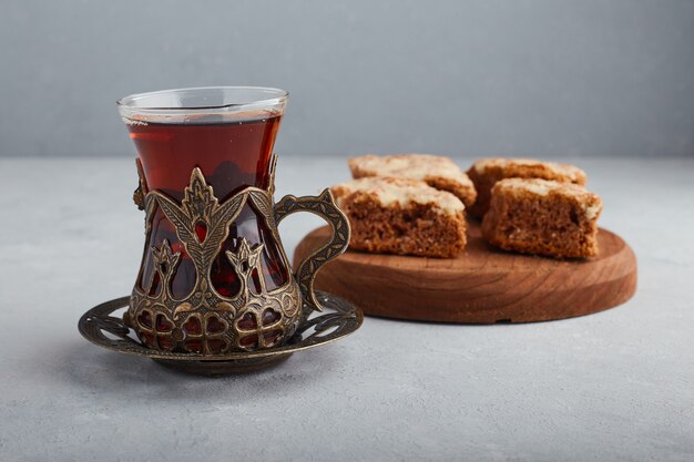 Geschnittene Torte auf einer Holzplatte mit einem Glas Tee.