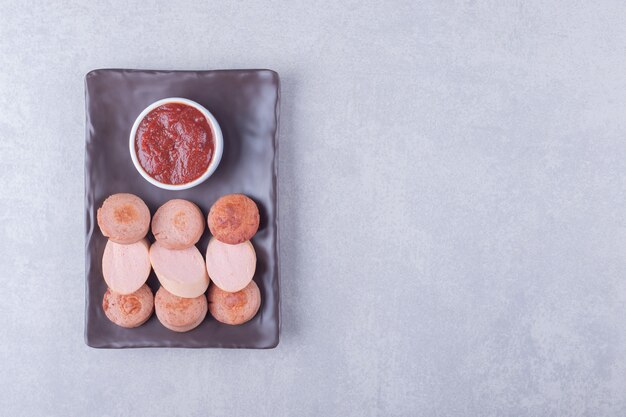 Geschnittene Würstchen mit Ketchup auf dunklem Teller.