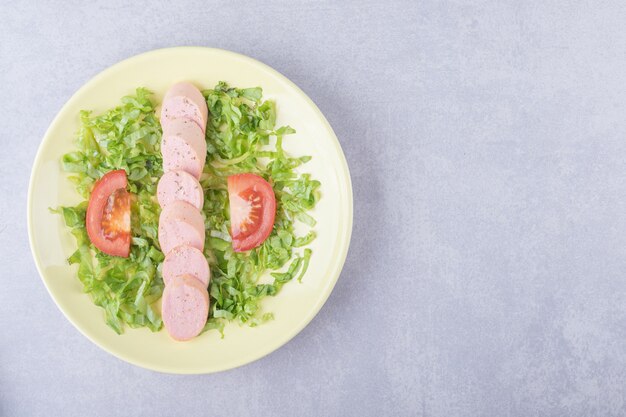 Geschnittene Würste und Tomaten auf gelbem Teller.