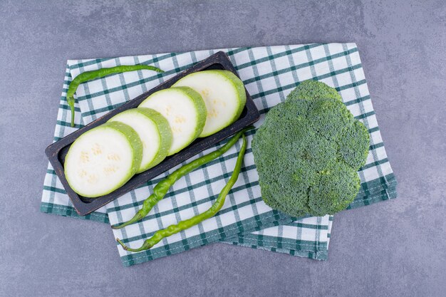 Geschnittene Zucchini, grüne Chilis und Brokkoli auf einem karierten Handtuch.