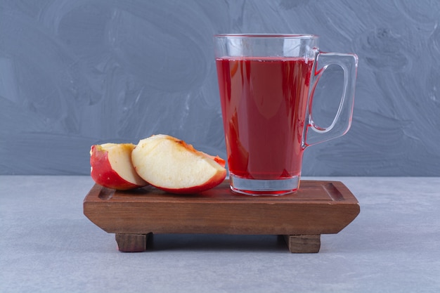 Geschnittener Apfel und ein Glas Kirschsaft auf einer Holzplatte auf Marmortisch.