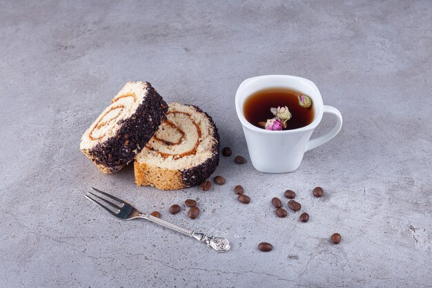 Geschnittener Brötchenkuchen auf Holzbrett mit Tasse Tee auf Steinoberfläche.