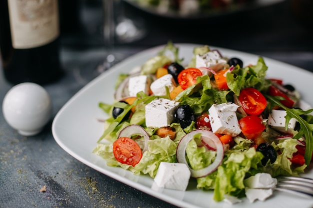 geschnittener Gemüse-Griechenland-Salat mit Käse-Olivenöl zusammen mit Rotwein auf Grau
