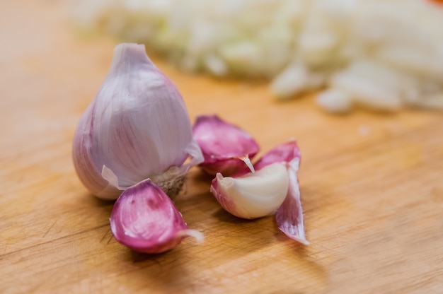 Geschnittener Knoblauch, Knoblauchzehe, Knoblauchbirne im Weidenkorb Platz auf Hackblock auf Vintage Holz Hintergrund