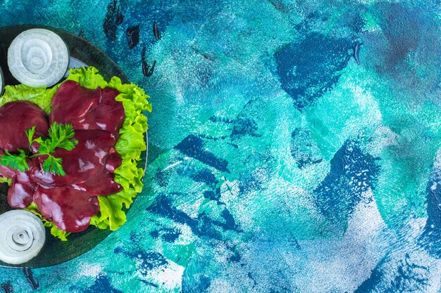 Geschnittener Rettich und Innereien auf einem Salatblatt auf dem Teller, auf blauem Hintergrund