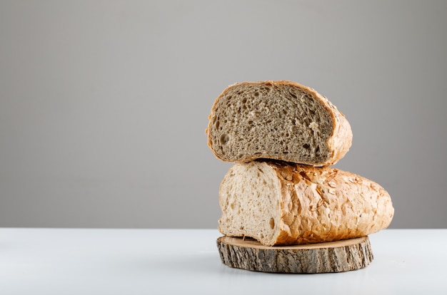 Geschnittenes Brot auf einem Holz auf einem weißen weißen Tisch und einer grauen Oberfläche. Seitenansicht. Platz für Text