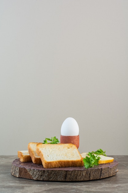 Geschnittenes Brot, Käse und gekochtes Ei auf einem Brett, auf dem Marmorhintergrund.