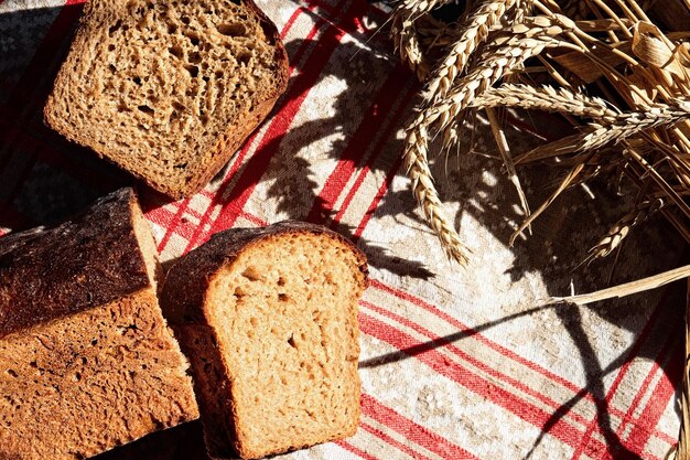 Geschnittenes Sauerteigbrot auf rustikalem rotgrauem Küchentuch und Ährchen aus Weizen. Tischplatte mit natürlicher Sonneneinstrahlung