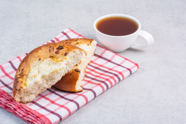 Geschnittenes süßes Brötchen auf einem Handtuch neben einer Tasse Tee auf dem Marmor.