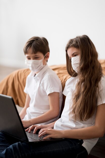 Geschwister mit Maske mit Laptop