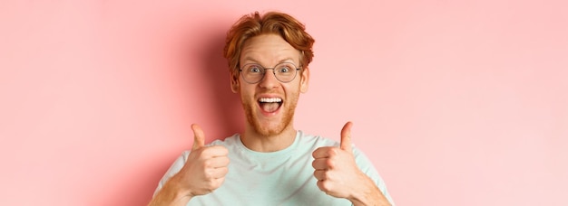Kostenloses Foto gesicht eines glücklichen rothaarigen mannes mit brille und t-shirt, der daumen hoch zeigt und aufgeregt aussieht, genehmigt und pra