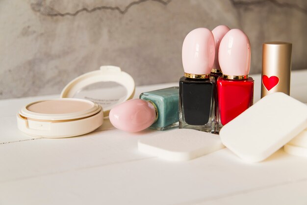 Gesichtskosmetik-Kompakt-Make-up-Pulver mit Schwämmen; Nagellackflasche und Lippenstift auf dem Tisch