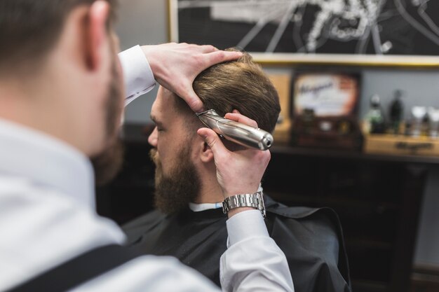 Gesichtsloser Friseur, der Haar des Mannes rasiert