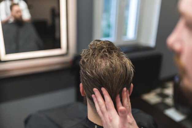 Gesichtsloser Friseur, der Mousse auf Haar des Mannes anwendet