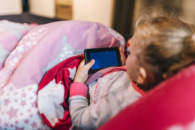 Gesichtsloses Mädchen mit Smartphone im Bett