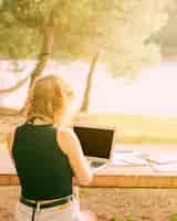 Kostenloses Foto gesichtsloses weibliches sitzen und arbeiten an laptop im malerischen platz