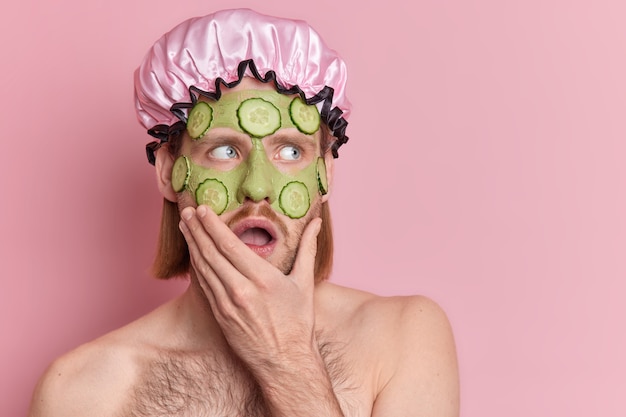 Gesichtspflegekonzept. Betäubter junger Mann trägt feuchtigkeitsspendende Schönheit auf Grüne Maske hält Kinnstarren überraschend beiseite