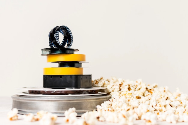 Kostenloses Foto gestapelt von den filmrollen mit filmstreifen auf die oberseite nahe dem popcorn gegen weißen hintergrund