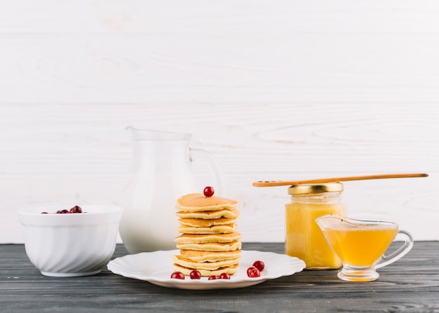 Gestapelt von den kleinen Pfannkuchen mit Beeren der roten Johannisbeere und Zitronenquark gegen weiße Wand