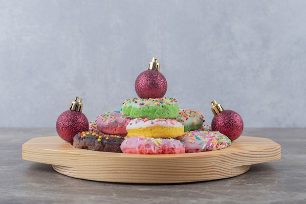 Gestapelte donuts und weihnachtskugeln auf einer holzplatte auf marmoroberfläche Kostenlose Fotos