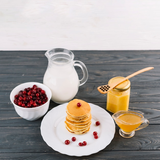 Gestapelte Pfannkuchen; Beeren der roten Johannisbeere; Milch- und Zitronenquark auf schwarzem Hintergrund aus Holz