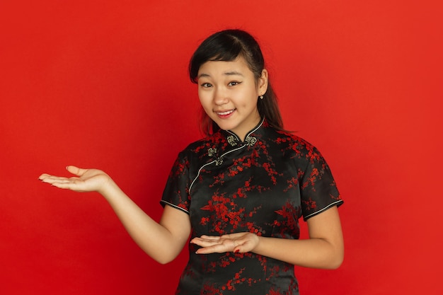 Gestikulieren, Gäste einladen. Frohes chinesisches neues Jahr 2020. Porträt des asiatischen jungen Mädchens auf rotem Hintergrund. Weibliches Modell in traditioneller Kleidung sieht glücklich aus. Feier, menschliche Gefühle. Copyspace.