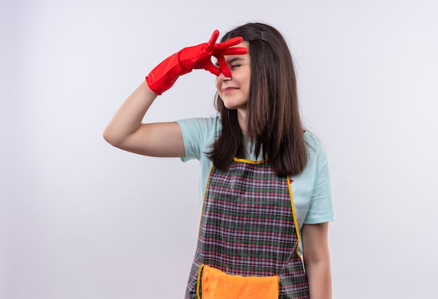 Gestörtes junges schönes mädchen, das schürze und gummihandschuhe trägt, die nase zwischen geschlossenen augen schließen