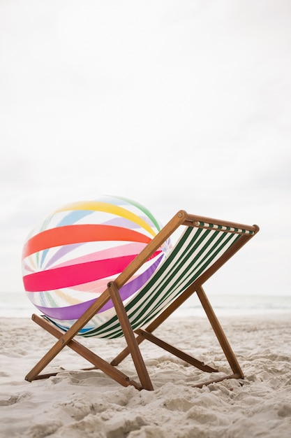 Kostenloses Foto gestreifte strandball gehalten auf leeren strand stuhl