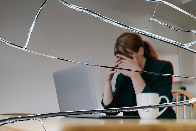 Gestresste Frau sitzt vor Laptop mit Rissglaseffekt