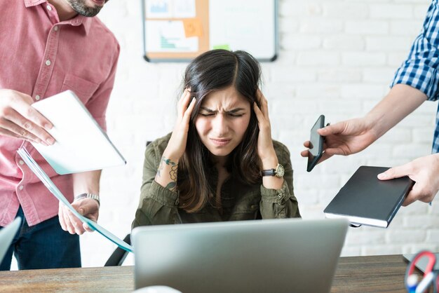 Gestresste Geschäftsfrau, umgeben von männlichen Kollegen, die Arbeit im Büro zuweisen