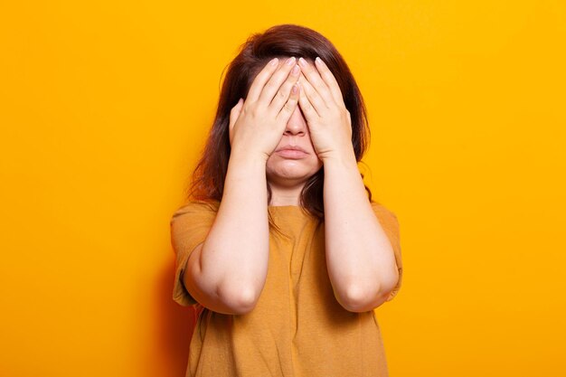 Gestresster Erwachsener bedeckt Gesicht und Augen mit Handflächen. Frau, die mit den Händen auf geschlossenen Augen steht und sich vor isoliertem Hintergrund emotional fühlt. Schüchterne Person, die den Gesichtsausdruck vor der Kamera versteckt