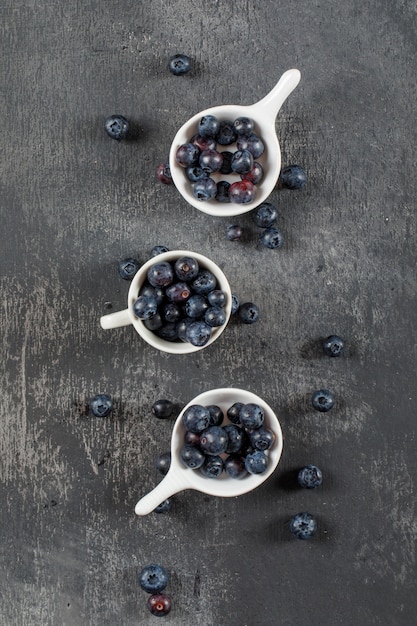 Gesunde Blaubeeren in Tasse und Schöpflöffel Draufsicht auf einer grauen Schmutzfläche